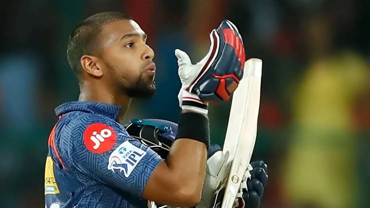 Cricketer kissing helmet in blue jersey, night match.